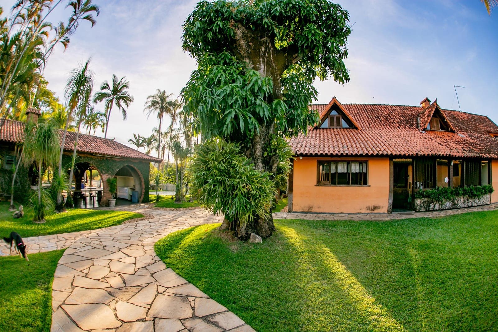 Fachada da casa principal com telhado de barro e caminho de pedra no gramado
