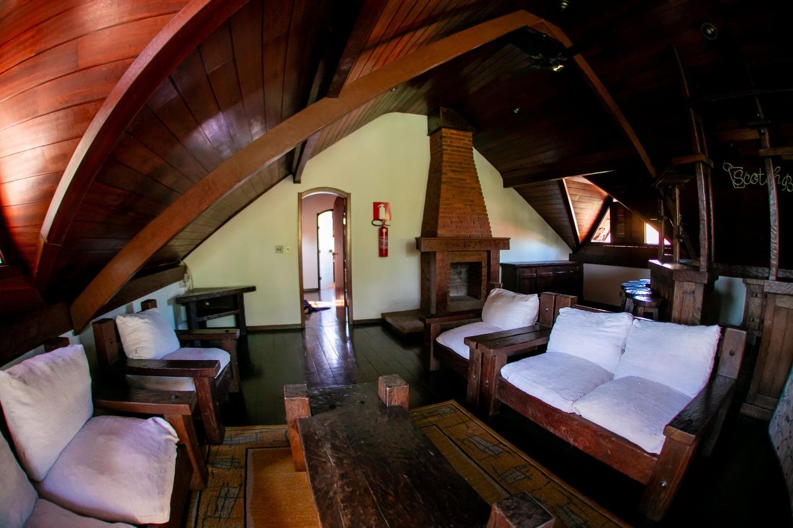 Sala com lareira de pedra, poltronas e estrutura aparente de madeira