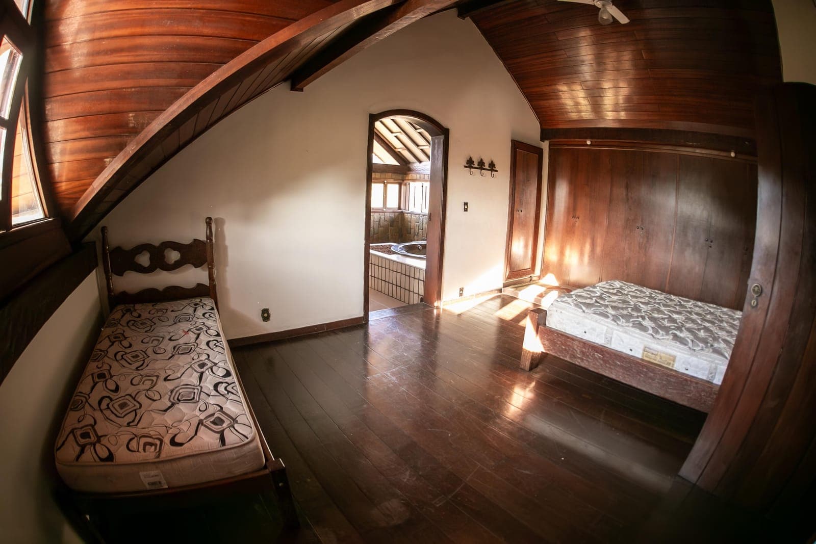 Quarto com paredes e teto de madeira, cama de casal arrumada