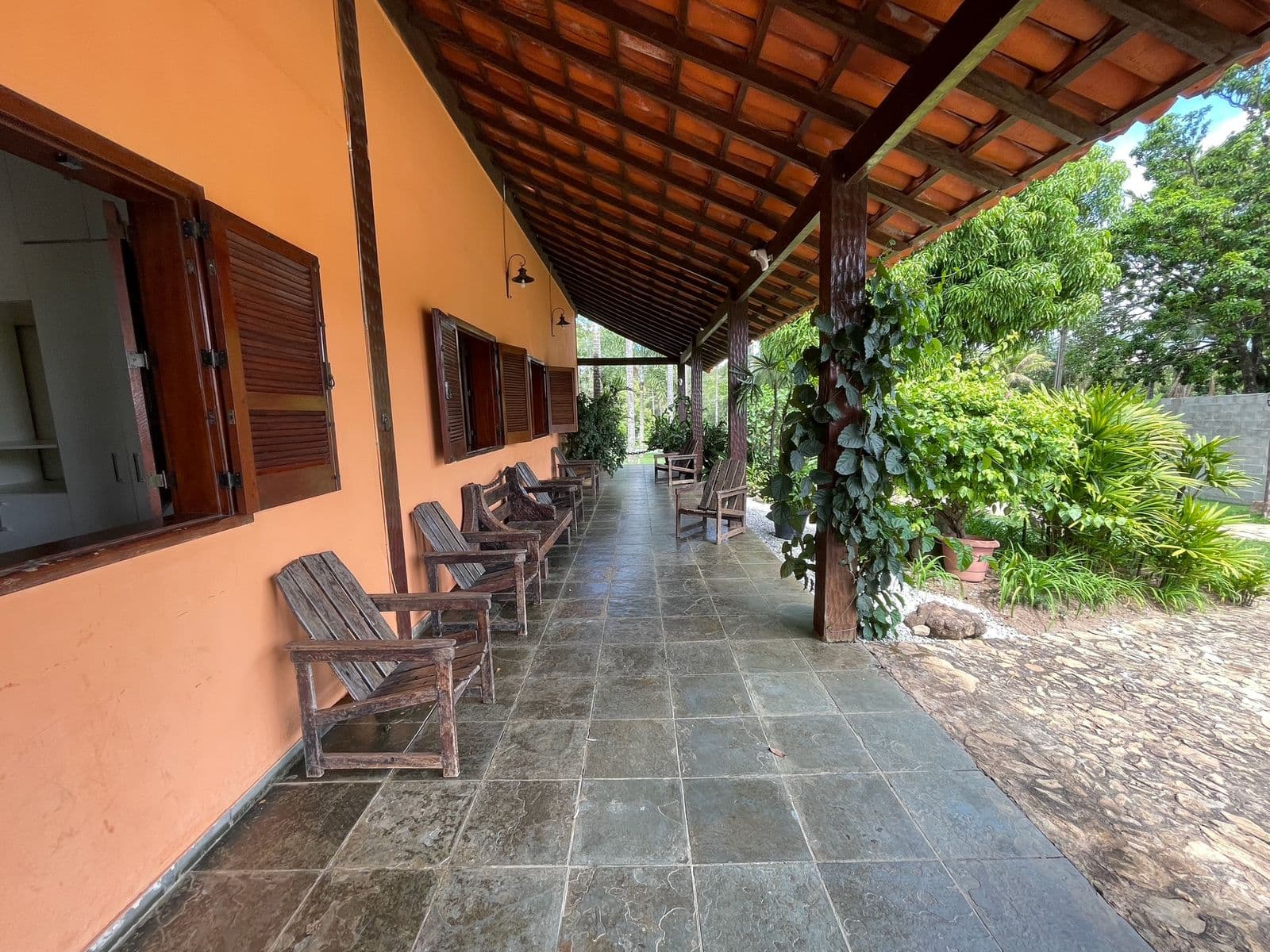 Varanda coberta com cadeiras de madeira ao longo da parede da casa