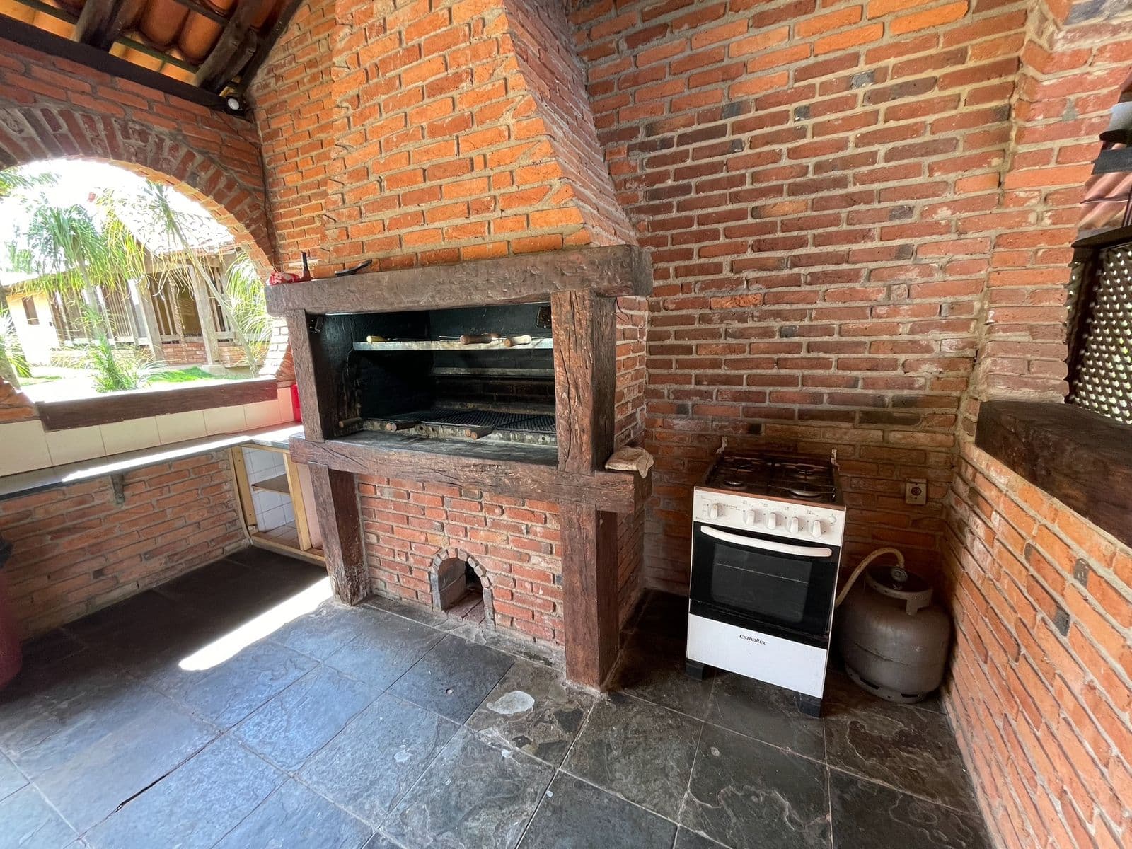 Churrasqueira de tijolo com grelha e fogão, aberta para o jardim
