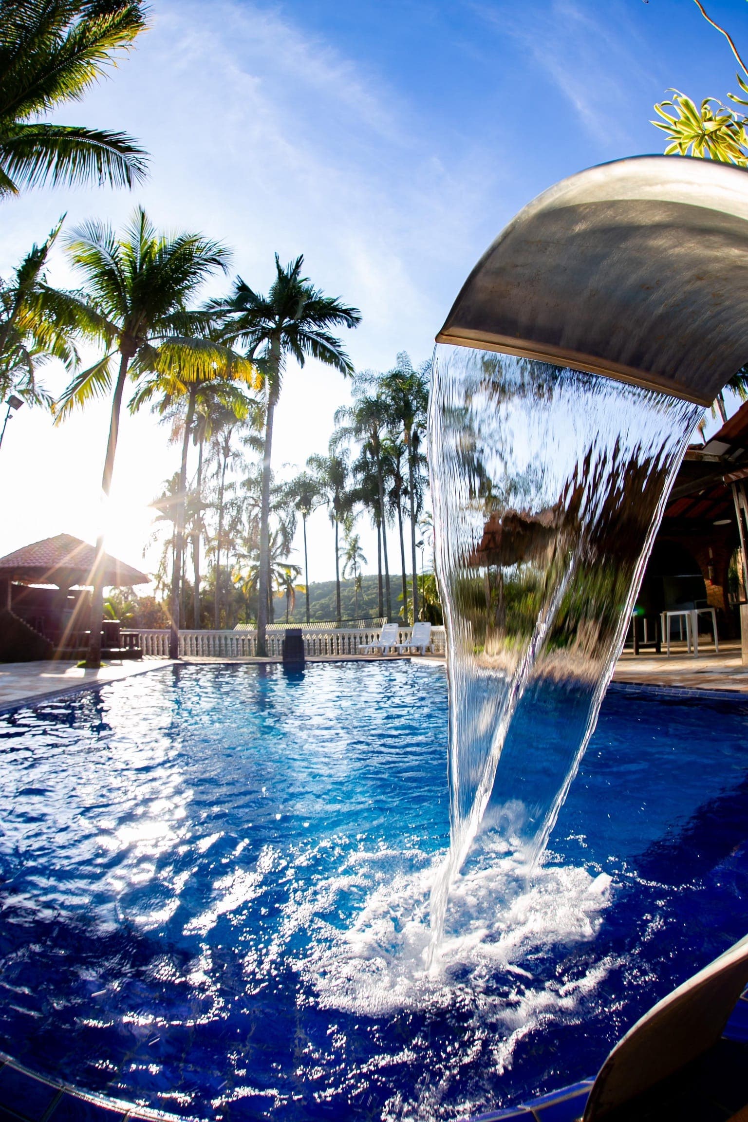 Cascata da piscina contra o sol, com palmeiras ao fundo no fim da tarde