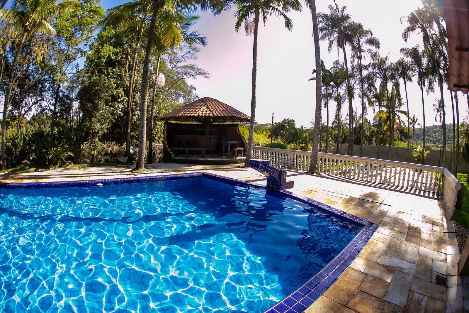Piscina com mureta de balaústres e o gramado do sítio logo atrás