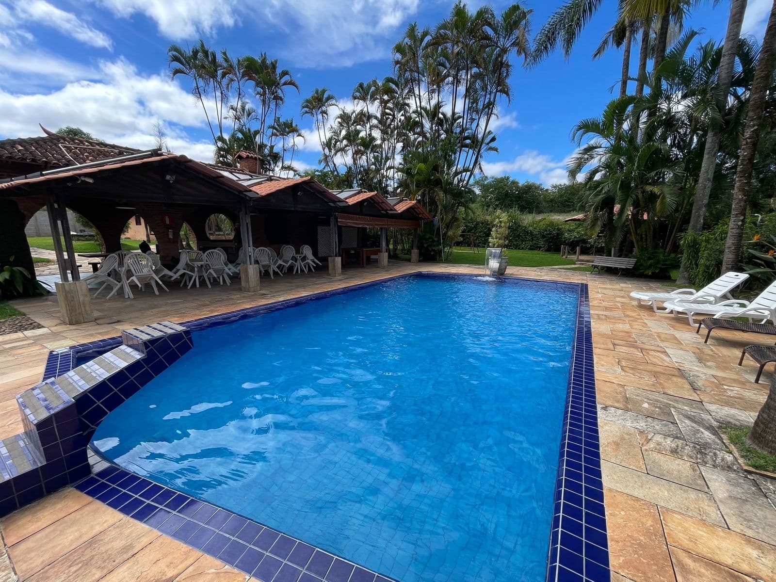 Piscina vista da área dos quiosques, com cadeiras e mesas na sombra