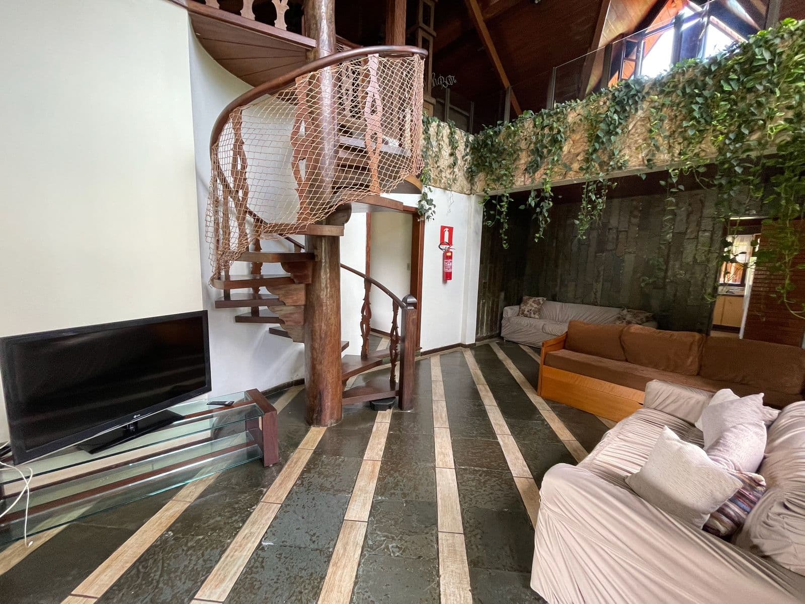 Sala de estar com escada caracol de madeira, sofás e TV