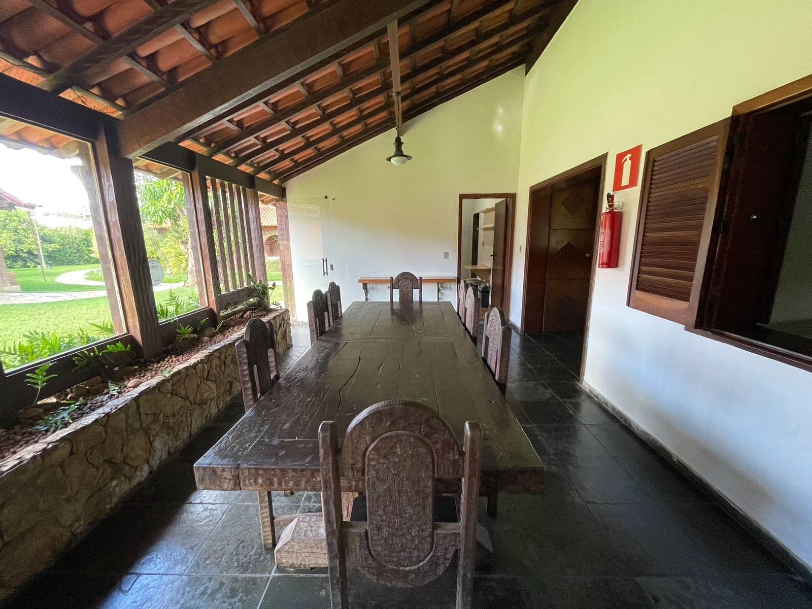 Mesa de jantar comprida de madeira, com janelões abertos para o gramado
