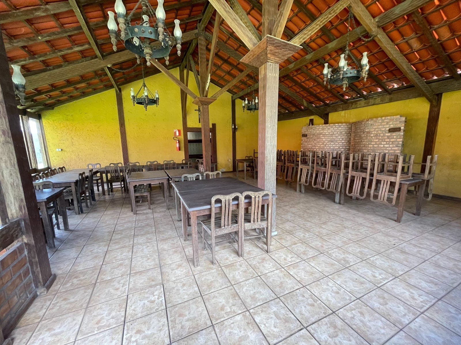Salão de festas com fileiras de mesas e cadeiras e churrasqueira ao fundo
