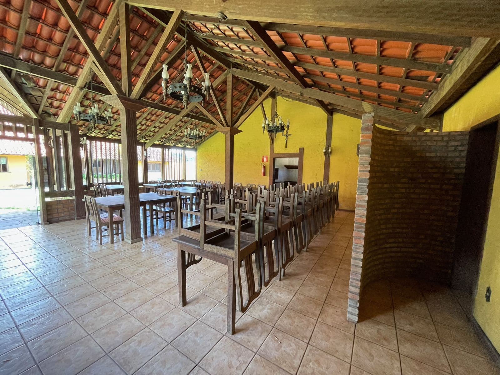 Salão de festas de outro ângulo, com as mesas e as cadeiras guardadas junto à parede de tijolo