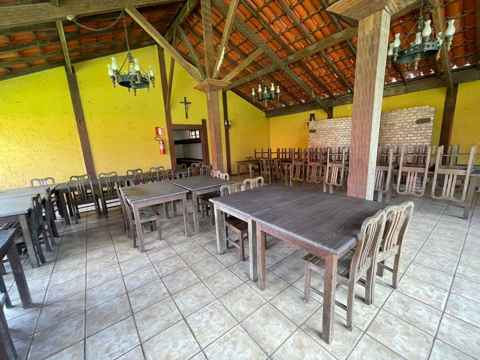Salão de festas coberto, com mesas, cadeiras e lustres de ferro no telhado de telha