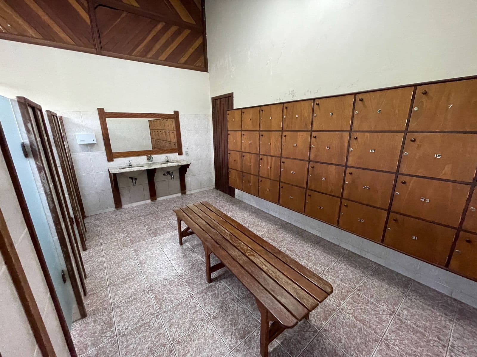 Vestiário com parede de armários de madeira, banco comprido e pias
